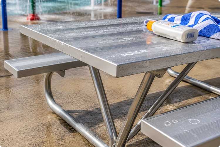 Wet aluminum picnic table near a splash pad showing exposure to water, sunscreen, and moisture in aquatic recreation areas.